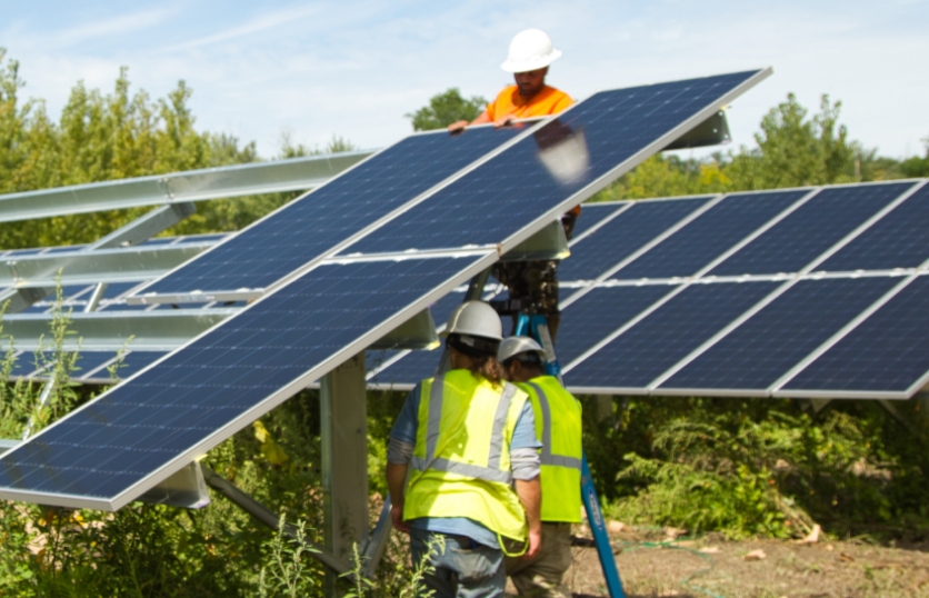 Nelnet Renewable Energy installer lifting a solar panel onto ground mount racking.