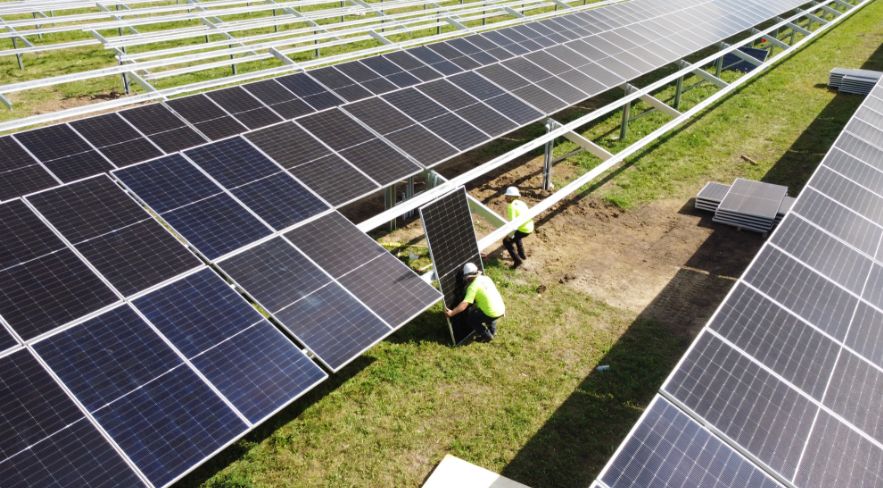 Nelnet Renewable Energy installer lifting a solar panel onto ground mount racking.