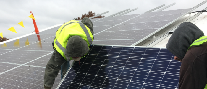 Two solar installers setting a module onto racking.