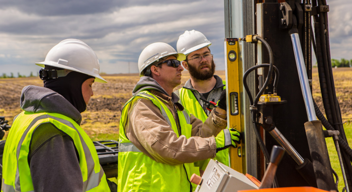 Three solar installers checking the level on a pile driver machine. 